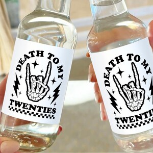 May include: Two clear glass bottles with white labels that say "Death to my twenties" in black text. The labels also feature a black and white illustration of a skeleton hand making a rock and roll hand gesture.