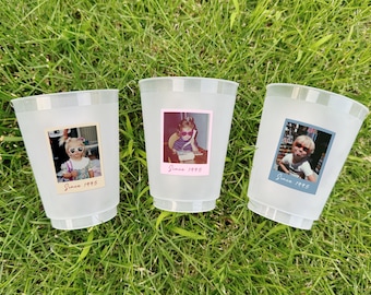 May include: Three frosted plastic cups with retro photos and the text "Since 1995" on the front. The cups are on a bed of green grass. Each cup has a different photo of a child wearing sunglasses.