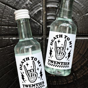 May include: Two clear glass bottles with white labels that say "Death to my Twenties" in black text. The labels feature a black and white illustration of a skeleton hand giving the rock and roll hand gesture.