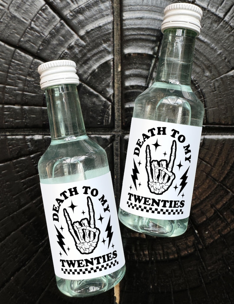 May include: Two clear glass bottles with white labels that say "Death to my Twenties" in black text. The labels feature a black and white illustration of a skeleton hand giving the rock and roll hand gesture.