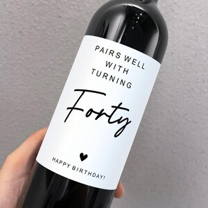 May include: A white wine bottle label with black text that reads "Pairs well with turning forty. Happy birthday!"