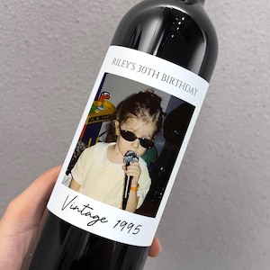May include: A wine bottle label with a photo of a young person wearing sunglasses and holding a microphone. The text on the label reads "Riley's 30th Birthday Vintage 1995".