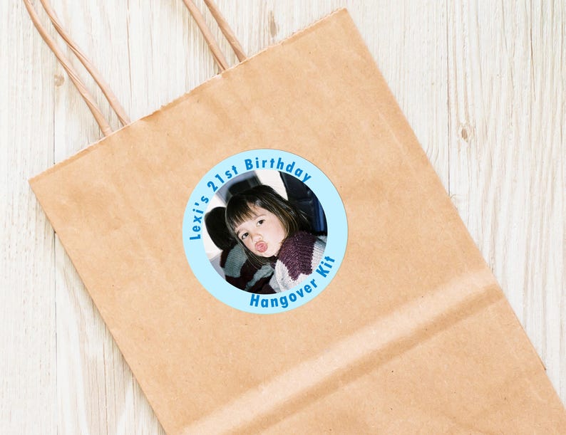 Op de afbeelding: Een ronde blauwe en witte sticker met een foto van een jong persoon in een auto. De tekst op de sticker luidt "Lexi's 21st Birthday Hangover Kit".