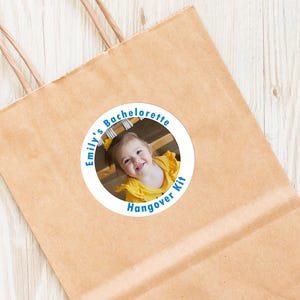 Op de afbeelding: Een ronde sticker met een witte achtergrond en blauwe tekst. De tekst luidt "Emily's Bachelorette Hangover Kit". In het midden van de sticker staat een foto van een jong meisje in een geel shirt.