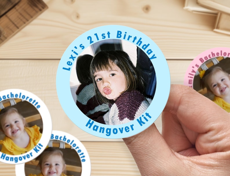 Op de afbeelding: Ronde blauwe en witte sticker met een foto van een jong persoon en de tekst "Lexi's 21st Birthday Hangover Kit".