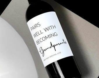 May include: A white wine bottle with a black label that reads "Pairs well with becoming grandparents" with the word "grandparents" in cursive. The label also includes the text "Baby Mike arriving June".