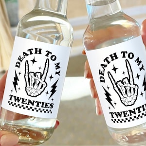 May include: Two clear glass bottles with white labels that say "Death to my twenties" in black text. The labels also feature a black and white illustration of a skeleton hand making a rock and roll hand gesture.