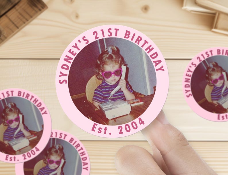 Op de afbeelding: Ronde roze sticker met een foto van een jong meisje dat een zonnebril draagt en een telefoon vasthoudt. De sticker zegt "Sydney's 21st Birthday Est. 2004".
