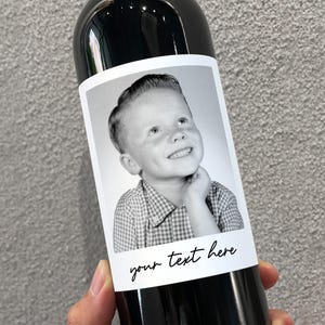 May include: A black and white photo of a young boy with a checkered shirt is on a wine bottle label. The label has the text "your text here" printed on it.