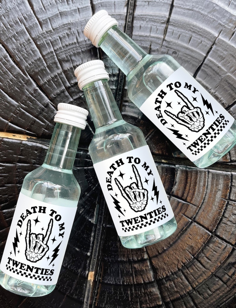 May include: Three small clear glass bottles with white labels that say "Death to my Twenties" in black text. The labels feature a black and white illustration of a skeleton hand making a rock and roll hand gesture with lightning bolts and stars.