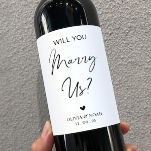 May include: A white wine bottle with a label that says "Will you marry us? Olivia & Noah 11.09.25".