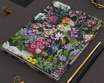 May include: A floral-patterned journal with a dark background, featuring a variety of colorful flowers in shades of pink, purple, white, and yellow. Gold and black pencils and paper clips are nearby. The journal's cover is filled with a vibrant botanical design.
