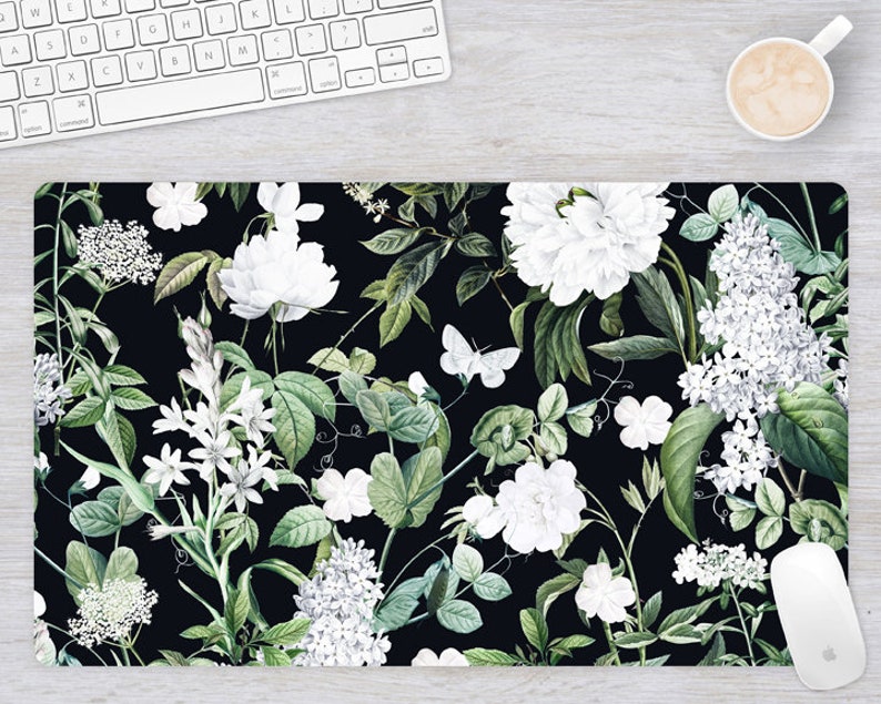 May include: A black background with a repeating pattern of white flowers and green leaves. The flowers are various types of white blossoms, including roses, peonies, and lilies. The leaves are a deep green and have a slightly textured appearance.