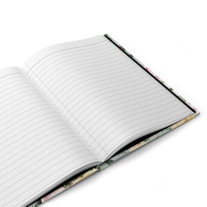 May include: Open notebook with lined pages. The cover features a floral design with pink, yellow, and green flowers. The notebook is open, revealing the blank, lined pages ready for writing.