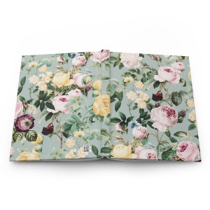 May include: Open journal with a floral pattern. The cover and inside pages feature a design of pink, yellow, and white roses, along with butterflies, on a light green background. The journal is open, displaying the detailed floral print.