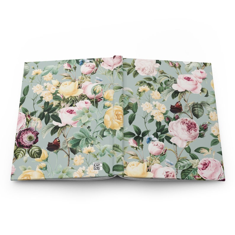 May include: Open journal with a floral pattern. The cover and inside pages feature a design of pink, yellow, and white roses, along with butterflies, on a light green background. The journal is open, displaying the detailed floral print.