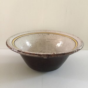 May include: A white ceramic bowl with a brown rim and yellow stripes. The bowl has a crackled glaze and is slightly chipped.