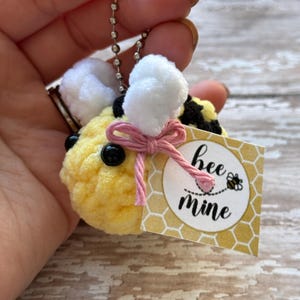 May include: A crocheted bee keychain with a pink bow and a tag that says "bee mine".