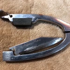 May include: A silver-colored, multi-tool pliers with a small knife blade and a sharpening stone. The tool is engraved with the words "Angler's Pliers".