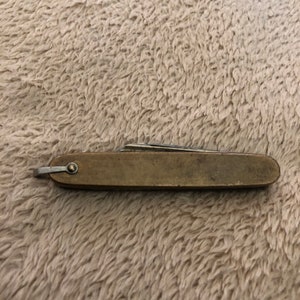 May include: A small, brass pocket knife with a single blade. The knife has a simple design and is in good condition.