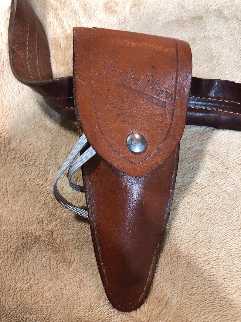 May include: A brown leather sheath with a silver button and the text "Angler's Piers" embossed on the front. The sheath is attached to a brown leather belt.