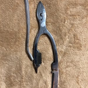 May include: Silver fishing pliers with a small knife attached. The pliers have a lanyard attached to them.