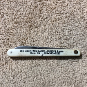 May include: A white pocket knife with a black handle and the text "TED CRUZ FARM LABOR - 26949 S. Lassen Huron, CA 209-945-9222" printed on the handle.