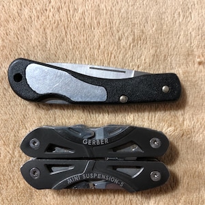 May include: Two multi-tools and a folding knife. The folding knife has a black handle with a silver blade. The multi-tools are black and silver, with the brand name "GERBER" and "MINI SUSPENSION-S" visible.