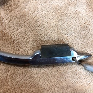 May include: A silver metal can opener with a black rubber grip. The opener has a small hole in the handle for hanging.