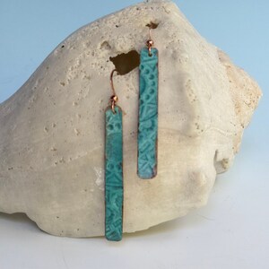 May include: A pair of turquoise blue earrings with a textured design. The earrings are made of metal and have a copper finish.