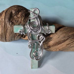 May include: A silver wire cross with a turquoise blue wooden base. The wire is twisted and curled into a decorative design.
