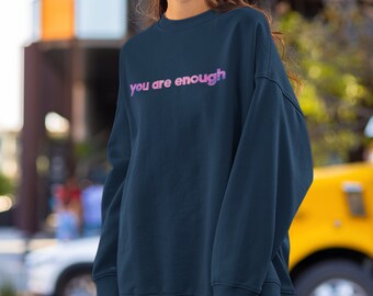May include: A navy blue sweatshirt with the text "you are enough" printed in a pink and purple gradient.