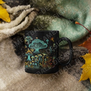 May include: A black ceramic mug with a design of colorful mushrooms on a dark background. The mug is surrounded by fall leaves and a fuzzy blanket.