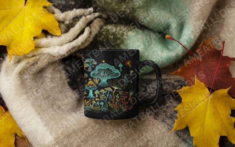 May include: A black ceramic mug with a design of colorful mushrooms on a dark background. The mug is surrounded by fall leaves and a fuzzy blanket.