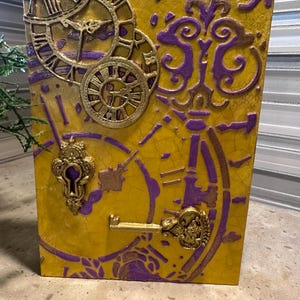 May include: A rectangular, yellow artwork with a cracked texture, featuring gold and purple clock faces, keys, and ornate embellishments. The design incorporates Roman numerals and decorative swirls, creating a vintage, steampunk aesthetic.
