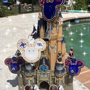 May include: A decorative model of Cinderella's castle with several Mickey Mouse-shaped keychains and ice cream bars. The keychains are navy blue and white with gold trim and red accents. The ice cream bars are brown with Mickey Mouse faces.