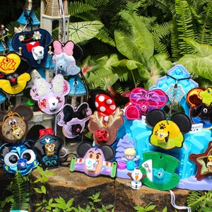 May include: A collection of colorful Disney character-themed pin trading lanyards. The lanyards feature various characters, including Mickey Mouse, Minnie Mouse, Donald Duck, Goofy, and others. The lanyards are made of fabric and have a metal clasp.