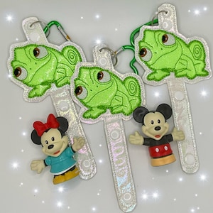May include: Three white fabric keychains with green embroidered chameleon designs and a Mickey Mouse figurine attached to one of the keychains.