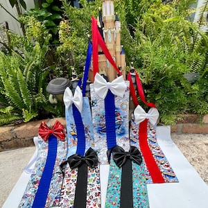 May include: A collection of colorful gift bags with various patterns and ribbon accents. The bags feature designs with cartoon characters and nautical themes. Each bag has a contrasting ribbon and bow, with colors including red, blue, black, and white.