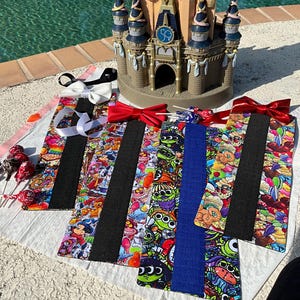 May include: Four colorful bow ties with a black and white stripe down the center. The bow ties feature a variety of Disney characters, including Mickey Mouse, Monsters Inc., and Toy Story. The bow ties are displayed on a table in front of a miniature castle.