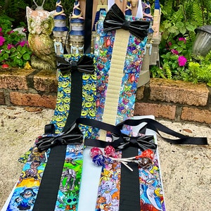 May include: Four colorful fabric pouches with black bow ties and black straps. Each pouch has a different cartoon character print. The pouches are hanging on a white surface.