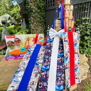 May include: Three vertical fabric door hangers featuring Disney cruise-themed patterns with Mickey and Minnie Mouse, anchors, and life preservers. Each hanger has a solid colored fabric strip and a white bow at the top, displayed near a Moana toy set.