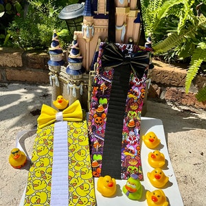 May include: Two bow ties, one with a yellow duck pattern and a yellow bow, the other with a colorful cartoon pattern and a black bow.  There are also several yellow rubber duck toys.