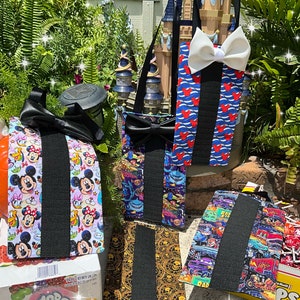 May include: Five different fabric pouches with black straps and bow ties. The pouches feature various Disney character prints, including Mickey Mouse, Minnie Mouse, and characters from The Little Mermaid and Cars.