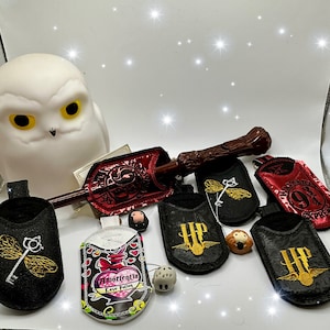 May include: A collection of Harry Potter themed accessories including a wand, a nightlight shaped like a snowy owl, and several small pouches with embroidered designs. The pouches feature the Hogwarts Express logo, a love potion, and the words "9 3/4" and "HP".