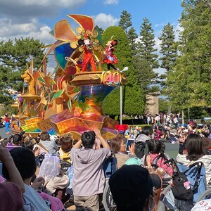 Puede incluir: Un carro aleg&oacute;rico colorido y elaborado con un gran dise&ntilde;o de molino de viento dorado. Mickey Mouse y Minnie Mouse est&aacute;n en el carro, saludando a la multitud. Las personas est&aacute;n sentadas en sillas de ruedas, viendo el desfile.