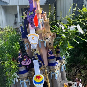 May include: A collection of colorful Disney character keychains featuring characters like Simba, Aladdin, and Buzz Lightyear. The keychains are attached to a miniature castle-shaped display.