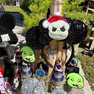 May include: Black and green Christmas themed Minnie Mouse ears with a Jack Skellington and Oogie Boogie design. The ears are decorated with silver glitter and a red Santa hat.