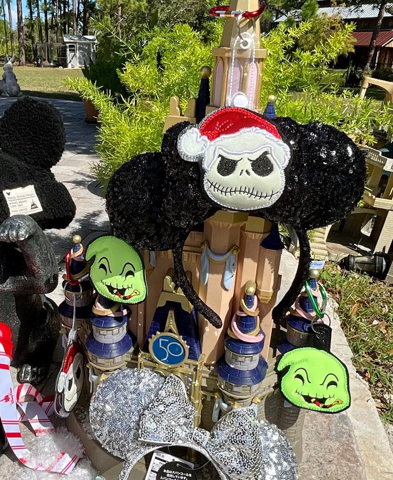May include: Black and green Christmas themed Minnie Mouse ears with a Jack Skellington and Oogie Boogie design. The ears are decorated with silver glitter and a red Santa hat.
