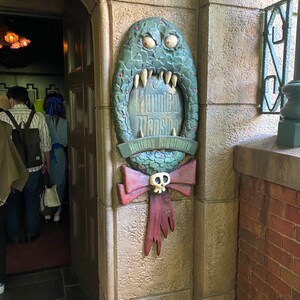 Może przedstawiać: Zielone, potworne usta z tabliczką z napisem "The Haunted Mansion Holiday Nightmare".